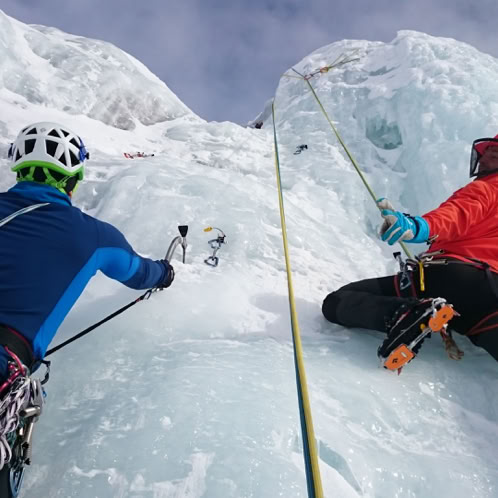 Two people climbing ice using crampons, ice axes and ropes