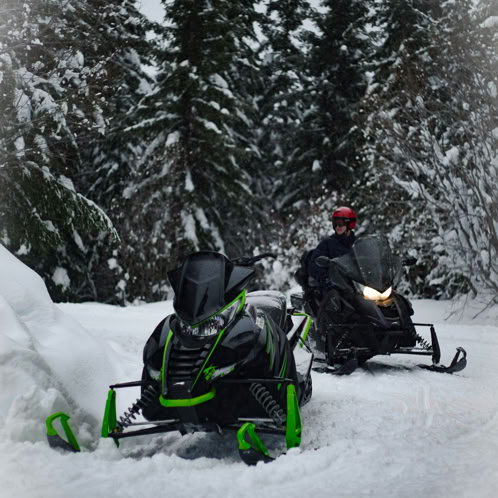 Two snowmobiles on trail with one unattended.